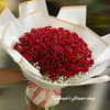 Large bouquet of red roses with white filler flowers wrapped in white paper and tied with a ribbon