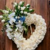 Heart-shaped ivory rose wreath with white orchids and blue hydrangeas on a wooden easel.