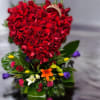 Tall arrangement with a heart of red roses above mixed colorful blooms and a gold tiara accent.