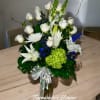 Tall arrangement of white roses and lilies with blue accents in a glass vase with a ribbon bow.