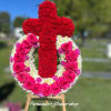 Standing funeral wreath of pink roses and white mums with a red carnation cross on an easel