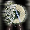Standing white funeral wreath with lilies, roses, and chrysanthemums on an easel with a white ribbon