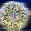 Large white floral wreath with roses and lilies displayed on a wooden easel