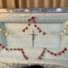 Red and white rosebud rosary draped inside a light blue open casket interior