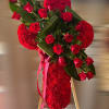 Standing red floral cross with red roses, large green leaves, and ribbon on a wooden easel.