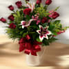 Tall arrangement of red roses and pink lilies in a white pitcher with a large red bow