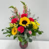 Mixed bouquet with sunflowers, hot pink roses, snapdragons, and daisies in a red glass vase