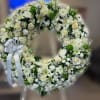 Large white and cream floral wreath with roses and lilies on a stand with a white bow