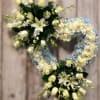 Heart-shaped wreath of white roses, lilies, and light blue hydrangeas on a stand