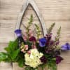 Wall-mounted rustic wooden frame planter with purple roses, white hydrangea, snapdragons, carnations, and green foliage.