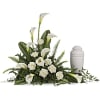 Sympathy arrangement of white calla lilies and roses beside a white cremation urn.
