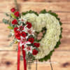 Standing heart-shaped white wreath with red roses and pink lilies on an easel with red ribbon