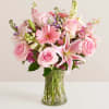 Pink roses, lilies, and mixed blooms arranged in a clear glass vase