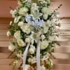 Tall white sympathy standing spray with roses, lilies, and mums accented by a white ribbon bow