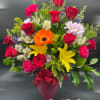 Mixed arrangement of red roses, yellow lilies, pink carnations and orange gerbera in a pink vase