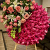 Large circular standing spray of hot pink roses with peach blooms and white lilies on a wooden easel