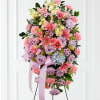 Standing spray of pink lilies, lavender roses, and carnations on an easel with lavender ribbon.