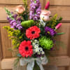 Mixed bouquet with pink roses, red gerbera daisies, green mums, and tulips in a glass vase with ribbon