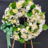 Standing wreath of white and pale yellow roses, lilies, and mums with a large green ribbon bow on an easel