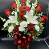 Tall arrangement of red roses, white lilies, and carnations in a glass vase with a red bow