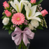 Mixed bouquet of pink roses, white lilies, carnations, and a gerbera daisy in a glass vase with a lavender bow.