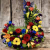Tall and low arrangement of bright roses, lilies, gerbera daisies, and other blooms in a rectangular container.