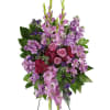 Tall standing spray of purple and pink flowers including roses on a metal easel