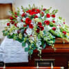Red and white casket spray of roses and mixed white flowers on a wooden casket