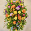 Tall multicolor standing spray with orange roses and yellow blooms on a metal easel