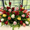 Low centerpiece of red, pink, yellow, and white roses arranged in a long, lush spray