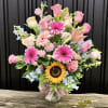 Tall mixed bouquet of pink roses and gerbera daisies with a sunflower in a glass vase