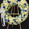 Large standing wreath of white and blue flowers with a white ribbon bow on a wooden easel
