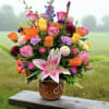 Colorful mixed bouquet of roses, lilies, and other blooms in a brown patterned ceramic pot.
