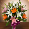 Bouquet of white, pink, and orange lilies in a glass vase with a purple ribbon