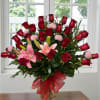 Bouquet of red roses and pink lilies in a glass vase with a red ribbon