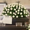 White rose casket spray on a dark casket with a white cloth drape