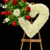 Heart-shaped white floral wreath on an easel with red roses and white flowers