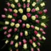 Tall standing spray of pink and pale yellow roses arranged on lush dark foliage