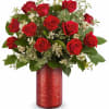Red roses arranged in a red vase with white filler flowers