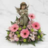 Pink gerbera daisies and lilies arranged around an angel figurine