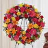 Colorful floral wreath on a black stand with roses, lilies, and daisies