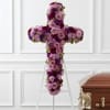 Purple and pink floral cross on a white easel beside a casket