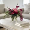 Pink and burgundy floral arrangement in a clear glass vase on a coffee table