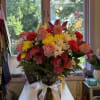 Mixed bouquet of pink roses, yellow and white daisies, and red carnations in a glass vase