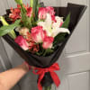 Bouquet of pink roses and white lilies wrapped in black paper with a red ribbon