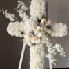 White floral cross on a stand with cream roses and dark accents