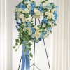 Heart-shaped floral wreath of white and blue flowers on a stand with a blue ribbon