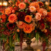 A large, lush centerpiece arranged on a gleaming gold pedestal vase, this