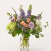 Mixed bouquet of roses, hydrangeas, and purple spikes in a clear glass vase