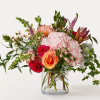 Mixed bouquet of pink, peach, and red flowers in a clear glass vase
